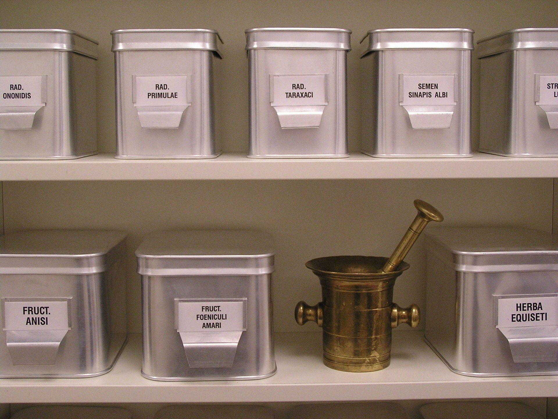 Museumsvitrinen mit beschrifteten Metallkästchen und einem Mörser mit Stößel aus Messing
