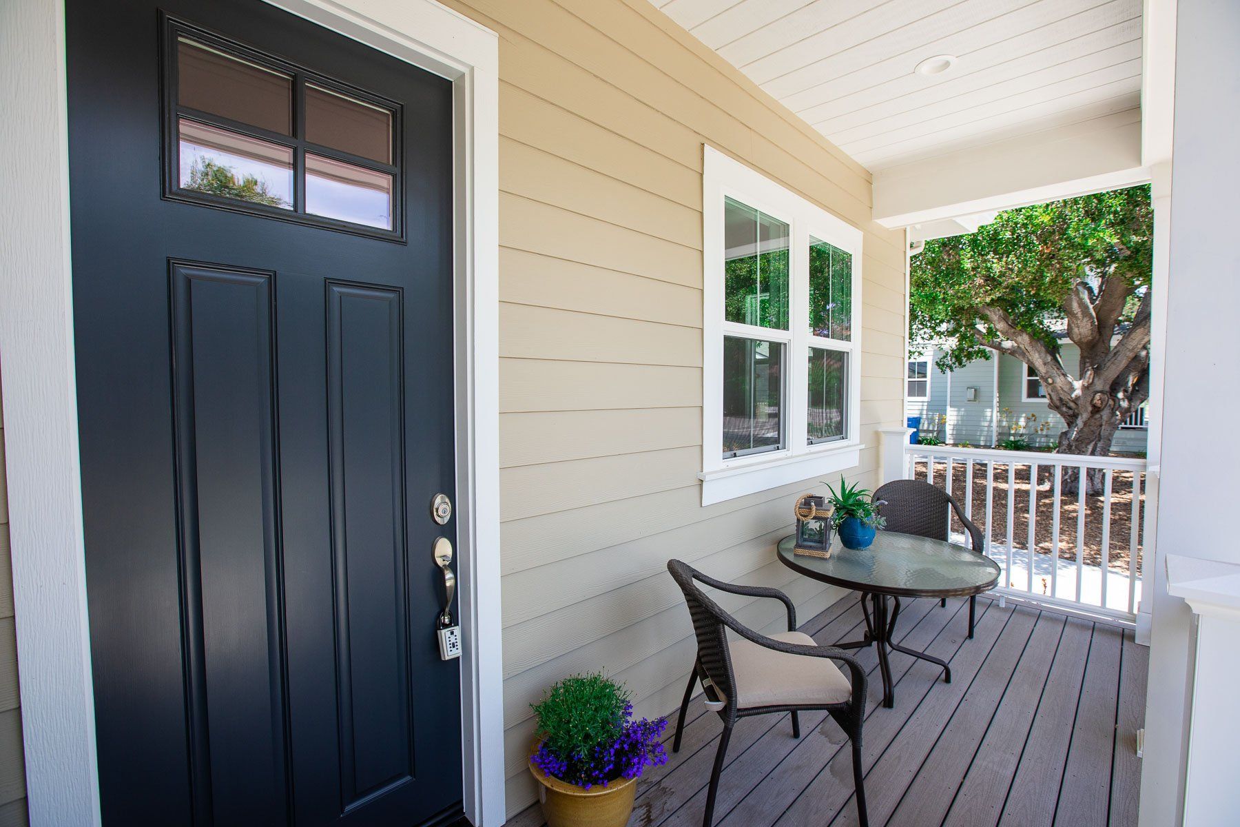A porch with a table and chairs and a black door.