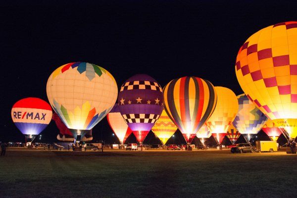 Hot air balloons lit up at night, various colors and patterns in a field.