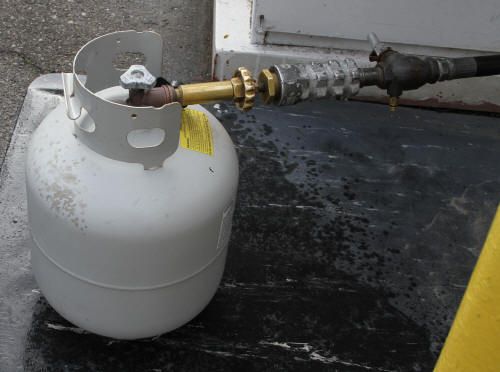 White propane tank connected to a hose on a dark surface.