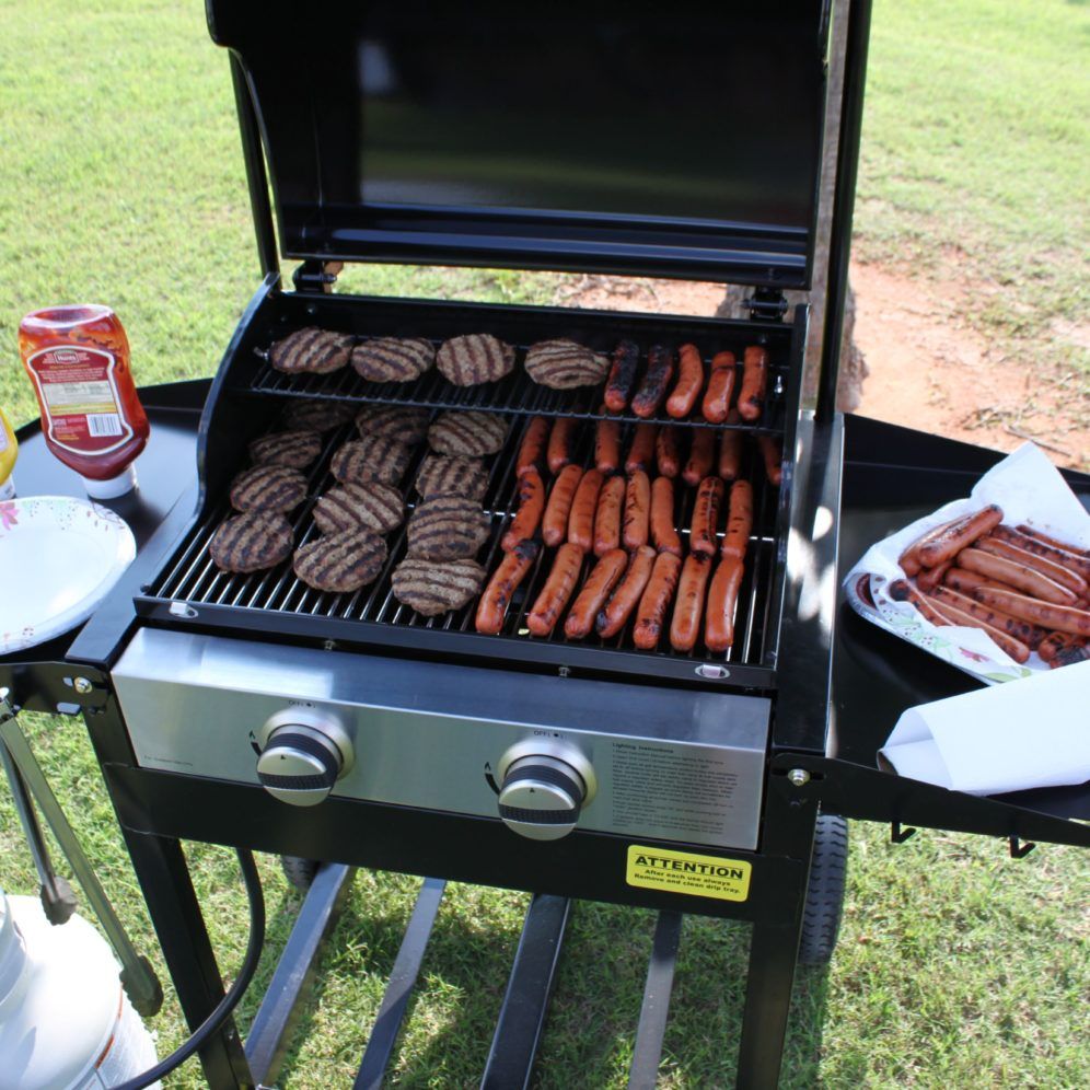 A grill with burgers and sausages cooking, with ketchup and a plate.
