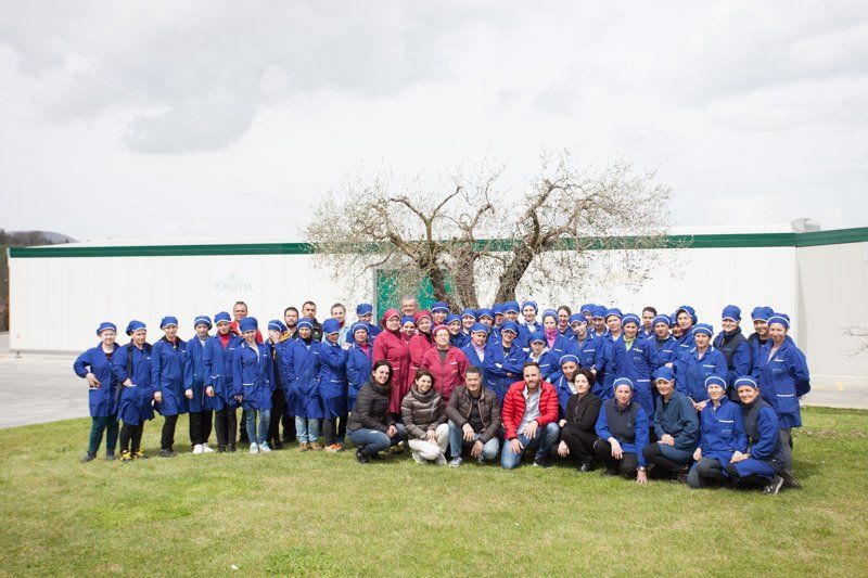 Un gruppo di persone in uniforme blu posa su un prato di fronte a un edificio bianco con un albero.