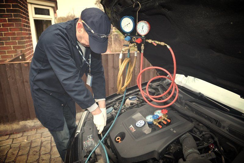 Technician working on a car engine with gauges and red hoses in a driveway