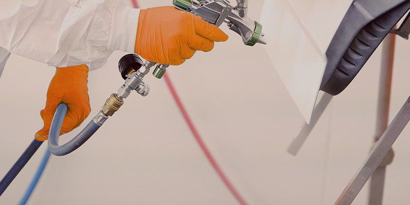 Orange-gloved hands spray-painting a wall with a paint gun and hose