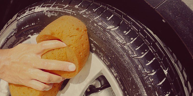 Hand scrubbing a car wheel rim with a sponge and soapy water