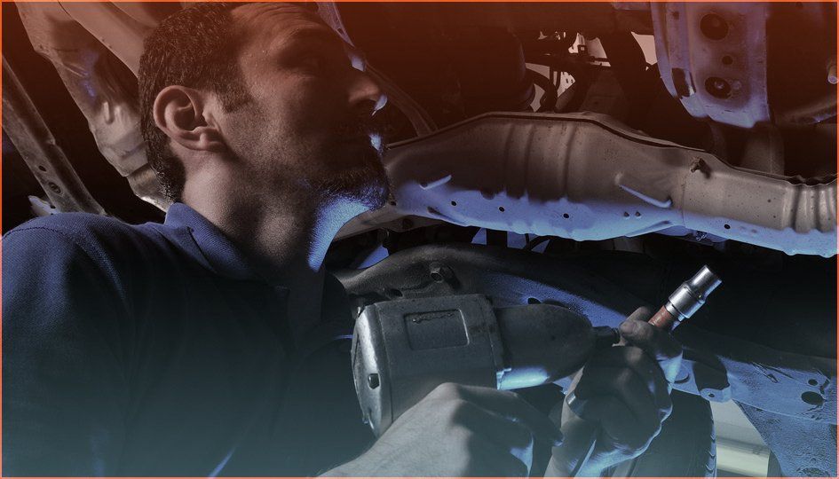 Mechanic using a tool under a vehicle in a dimly lit garage