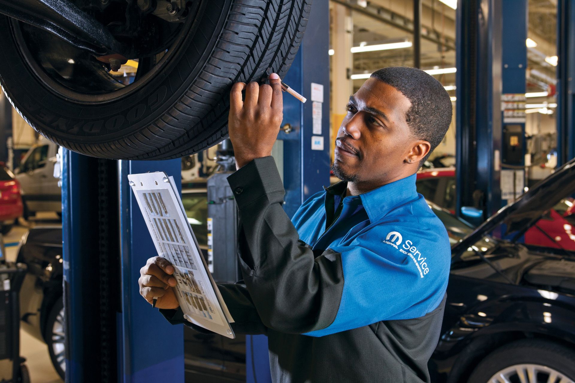 Mechanic in blue uniform inspecting a car tire in an auto repair shop