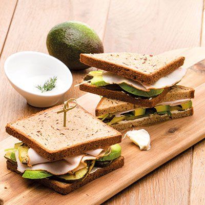 Twee sandwiches met kalkoen en avocado op volkorenbrood, geserveerd met een klein schaaltje dipsaus op een houten snijplank.