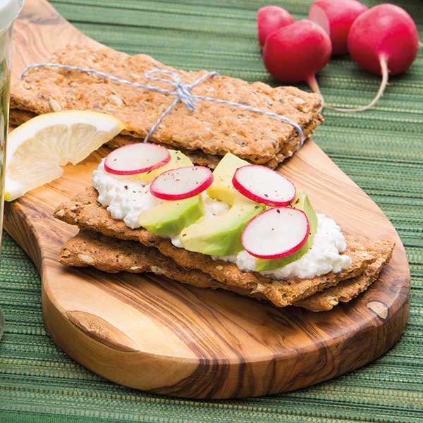 Knoflookbrood belegd met kwark, avocado en radijsschijfjes op een houten plank, met radijs en citroen ernaast.
