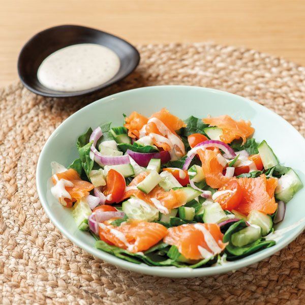 Een lichtgroene kom met salade van gerookte zalm, komkommer, tomaat en rode ui, geserveerd met een romige dressing.