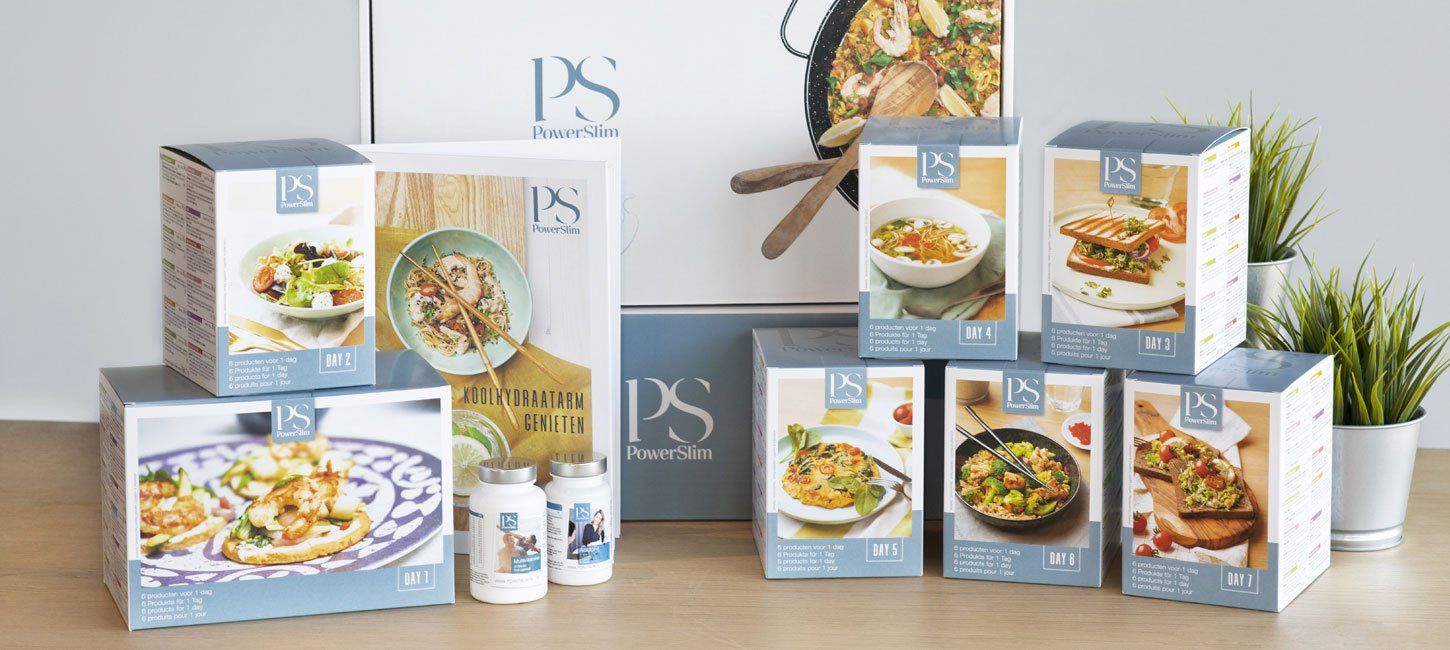 Een verzameling maaltijdpakketten, kruidenpotjes en een receptenboek van PS Life, uitgestald op een ondergrond met kleine plantjes.
