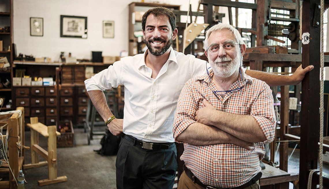 An older man and a younger man standing and smiling in a workshop