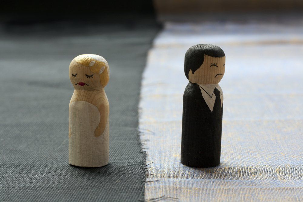 Two wooden dolls resembling a groom and bride frowning and facing away from each other