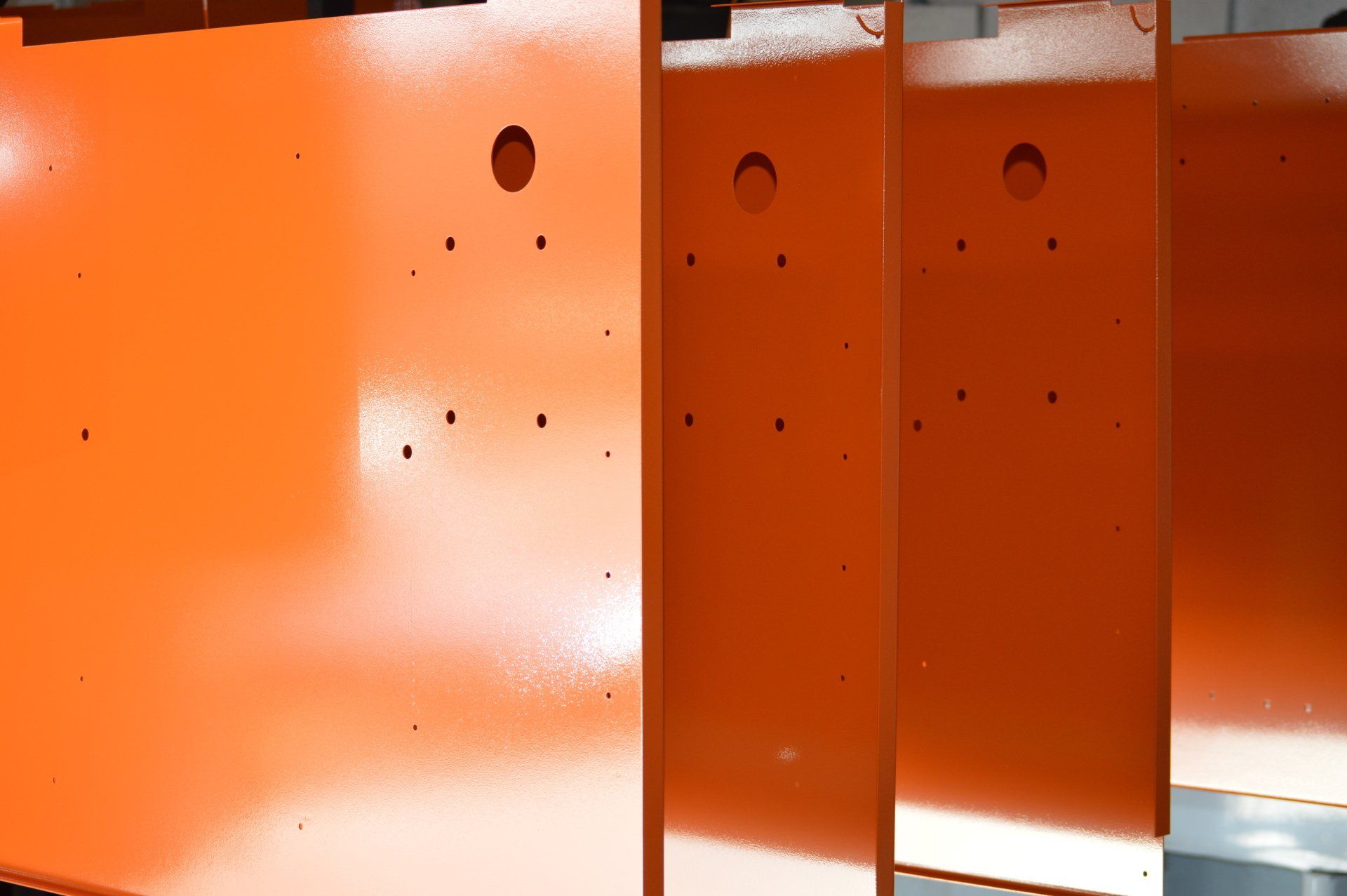 Three pieces of orange metal with holes in them are sitting next to each other.