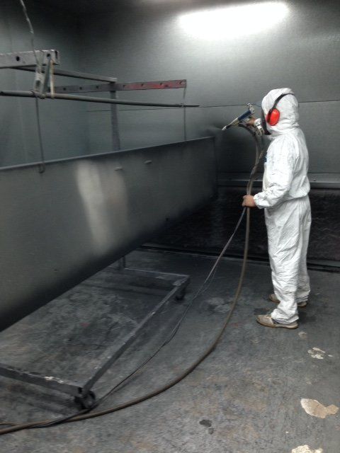 A man in a white suit is spraying a metal surface