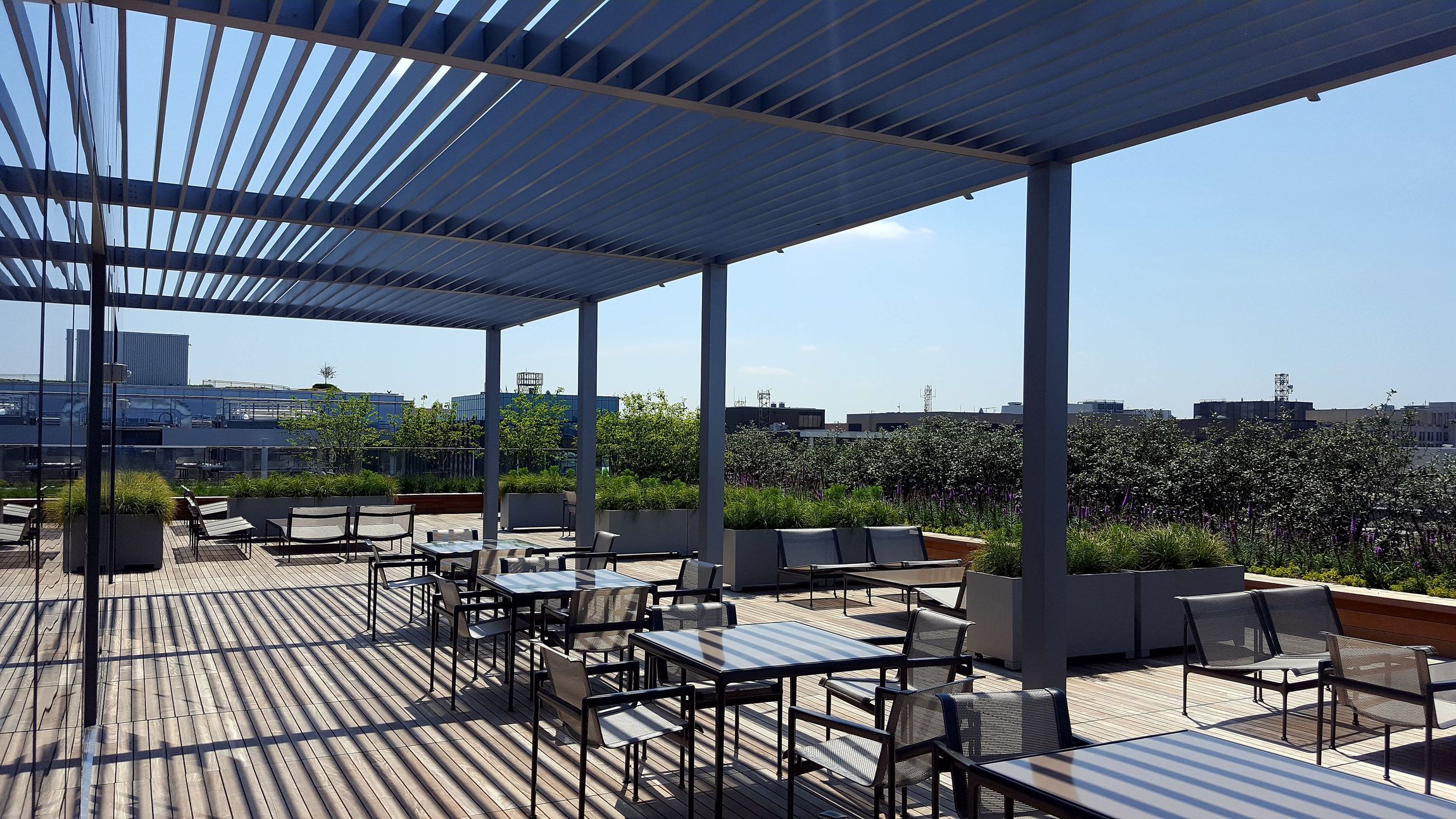 a patio with tables and chairs under a pergola on a sunny day .