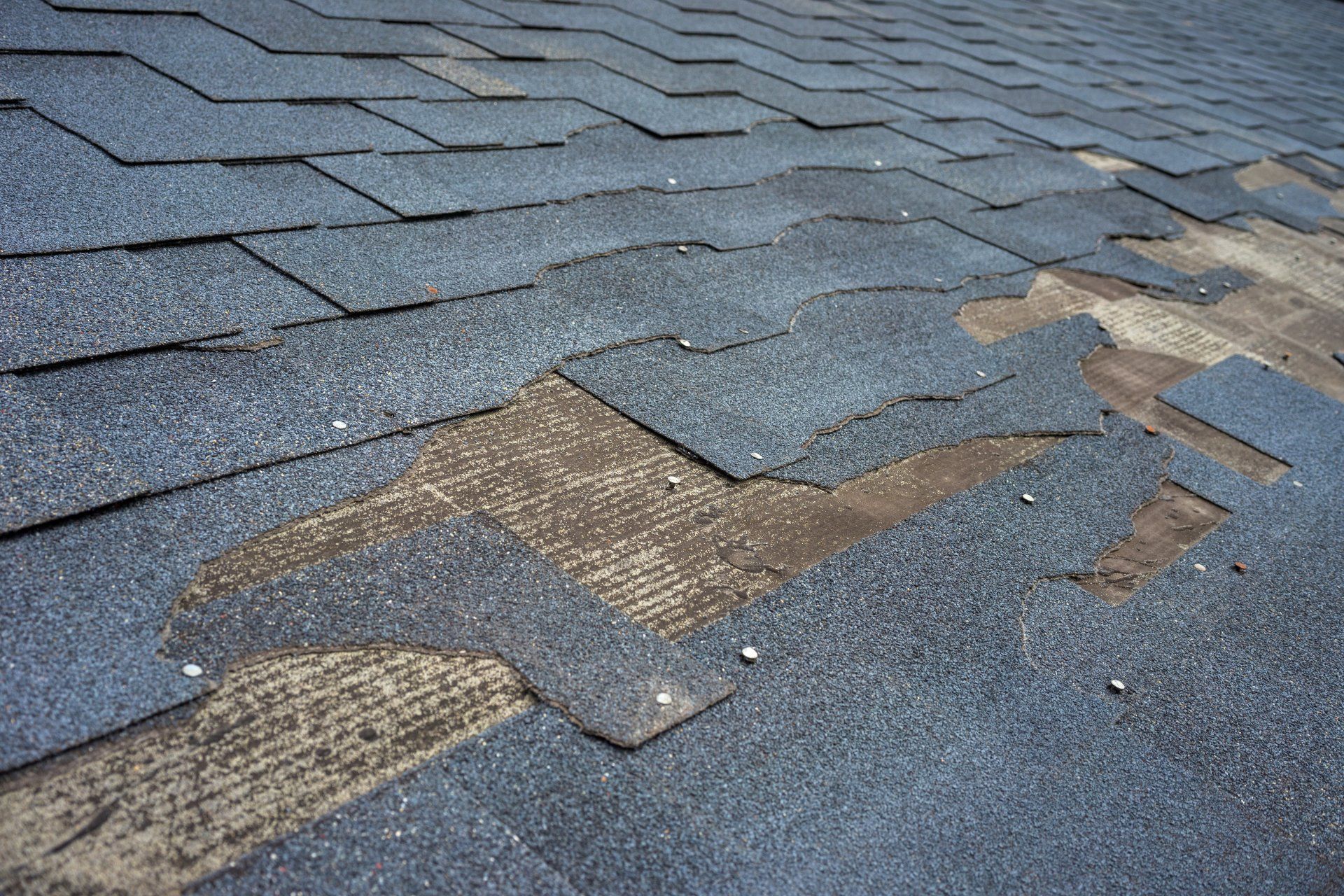 Damaged blue roof shingles with missing sections exposing the underlayment