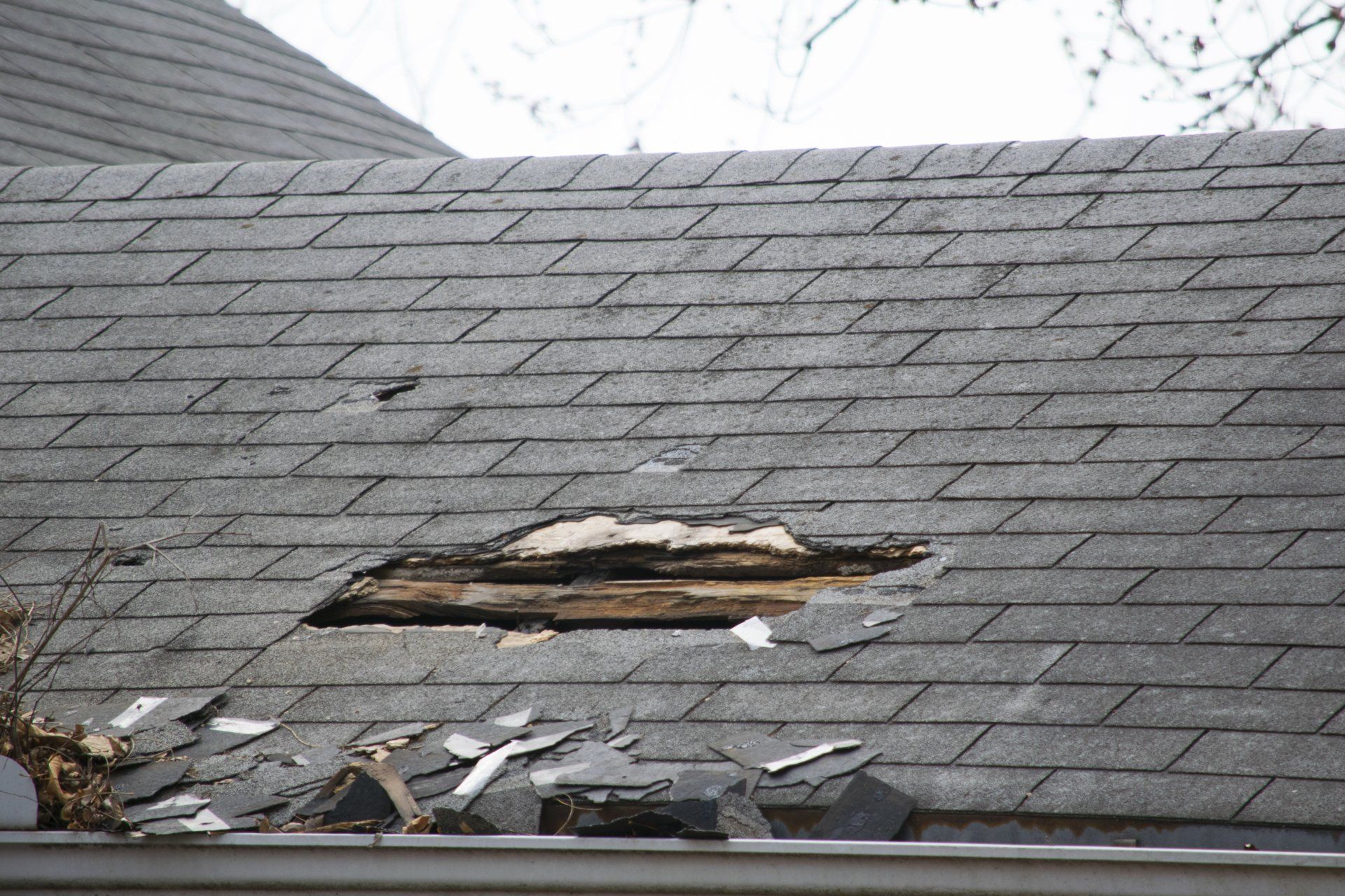 Damaged gray shingle roof with a large hole and debris in the foreground