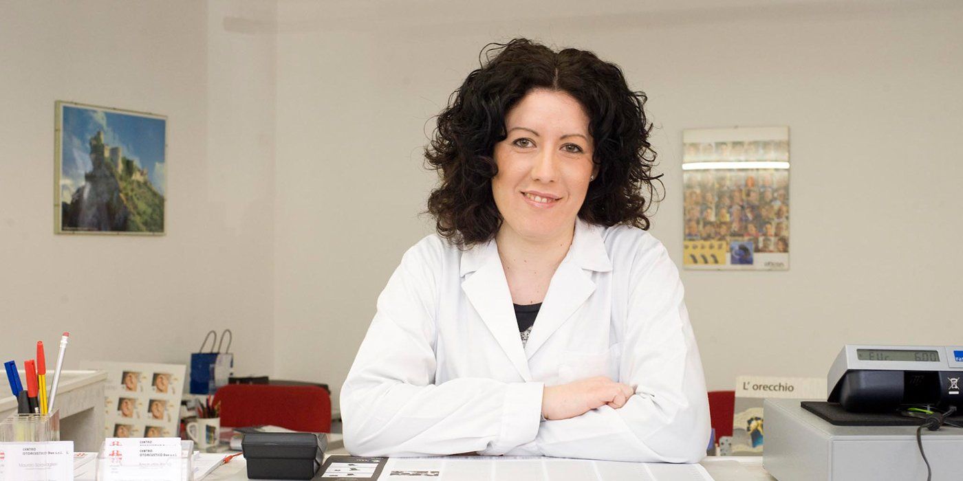 una donna con capelli neri ricci con camice bianco seduta a una scrivania 