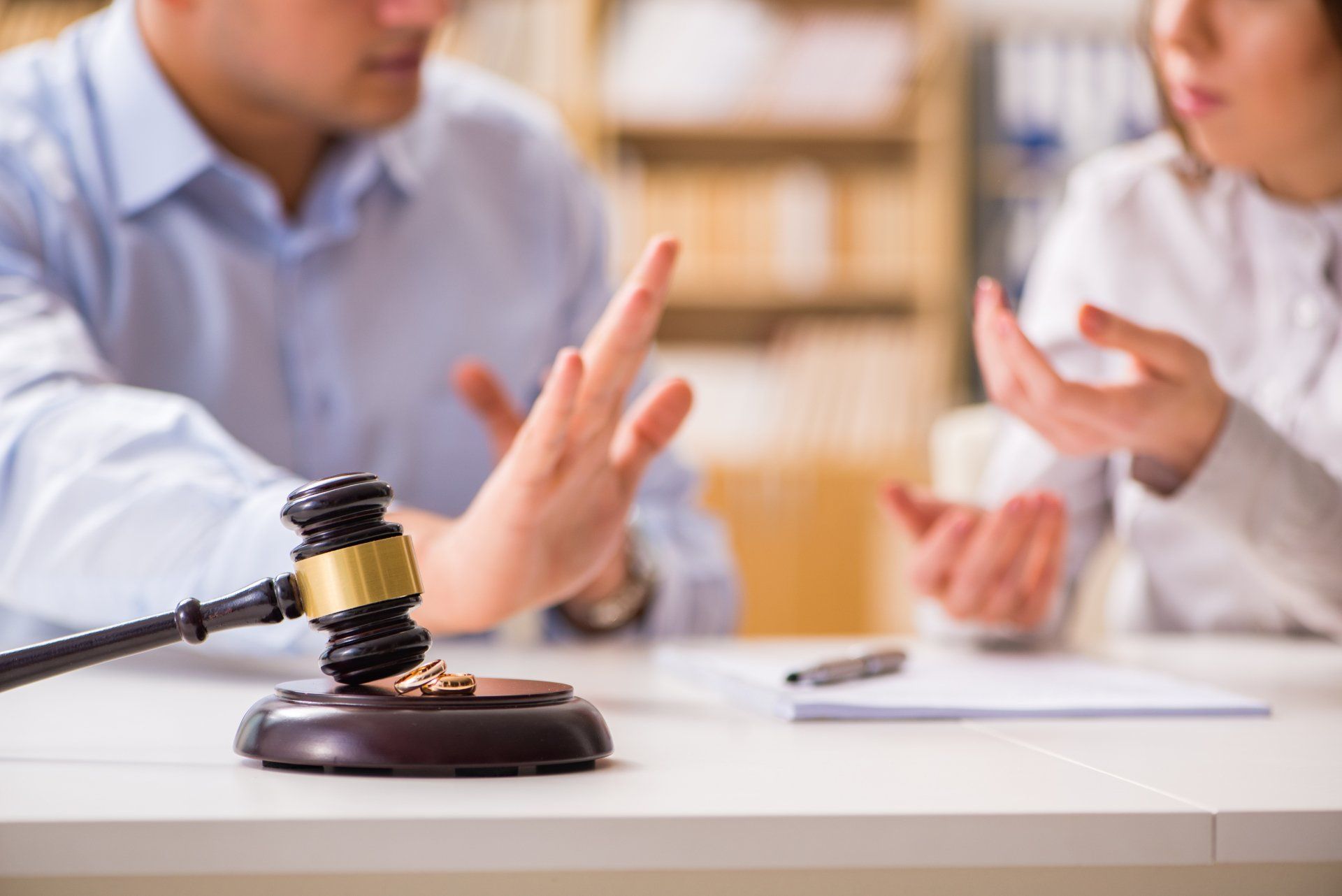 A man and a woman are sitting at a table with a gavel and wedding rings on it.