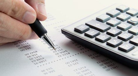 A hand using a pen on a sheet of figures, with a calculator nearby