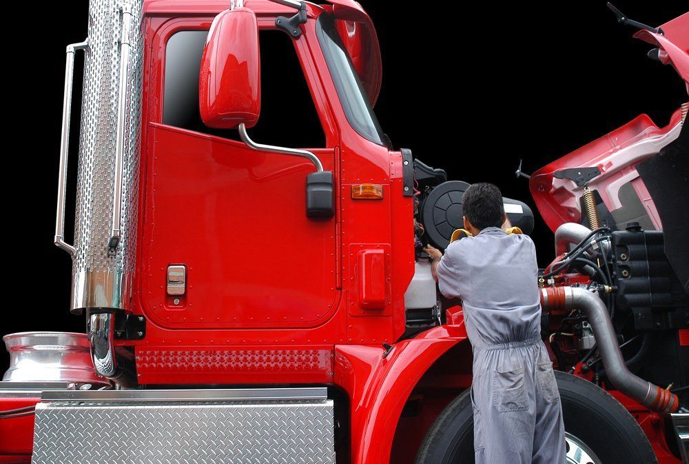 Mechanic in gray jumpsuit working on the red engine of a semi-truck.