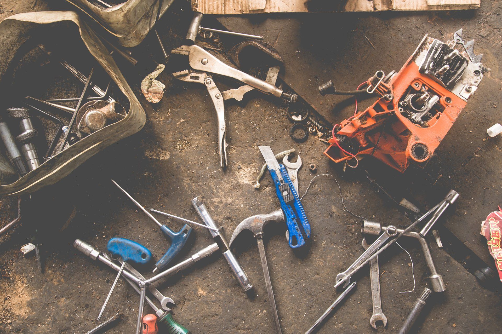 Tools scattered on a dusty concrete surface, including wrenches, pliers, and a chainsaw.
