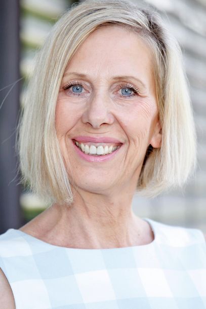 Eine Frau mit blonden Haaren und blauen Augen lächelt in die Kamera.