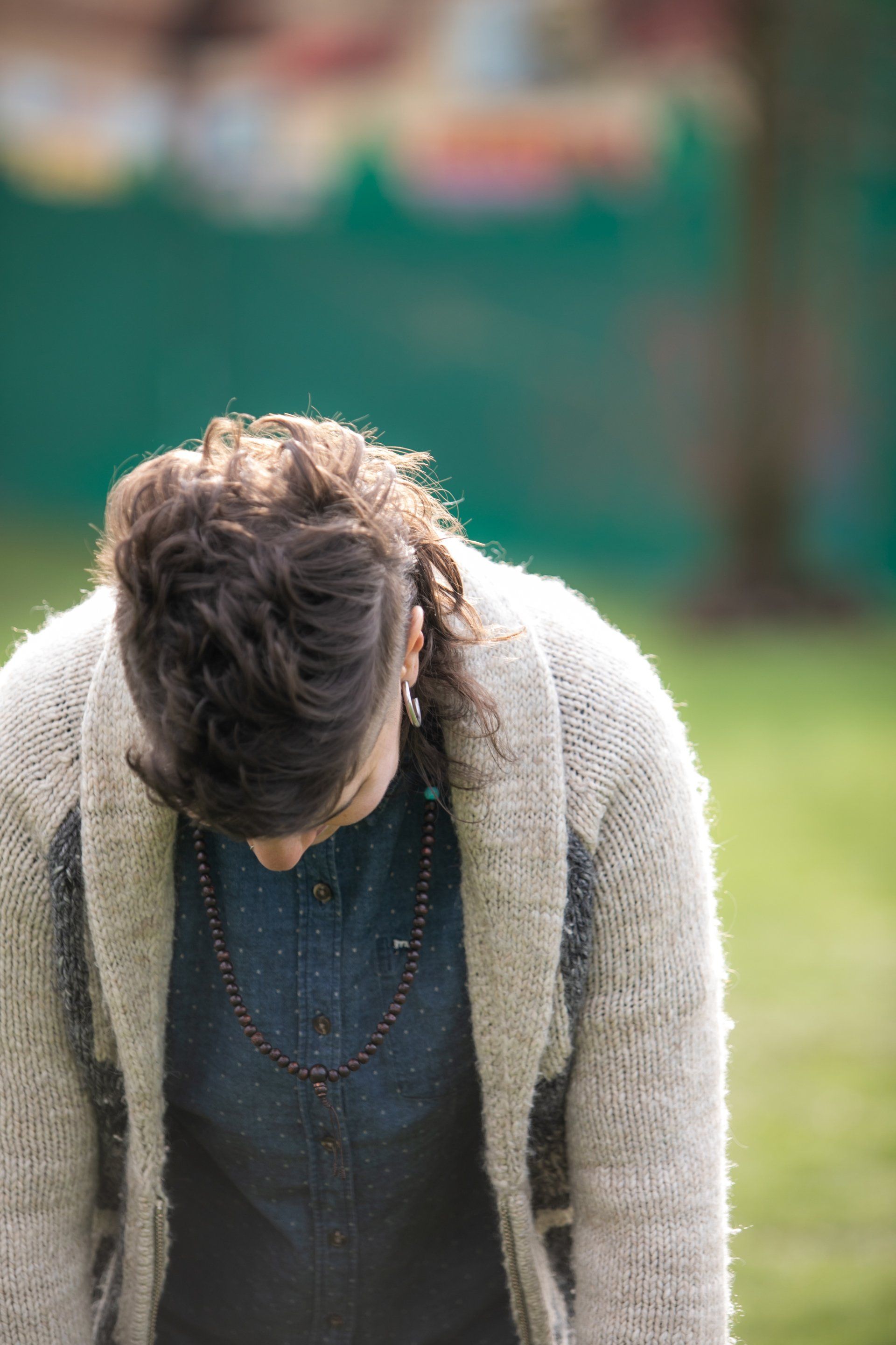 A person wearing a sweater and a denim shirt is looking down.
