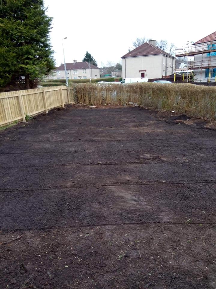 Empty fenced yard with dark soil, wooden side fences, and houses in the background.