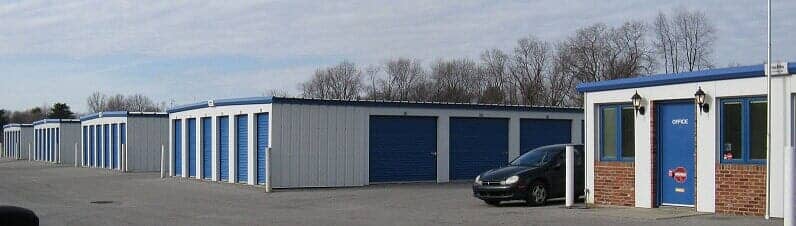 Storage units with blue doors, metal walls, and a car in front.