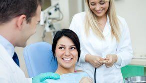 A young lady sitting in the chair, flanked by a dentist and dental nurse