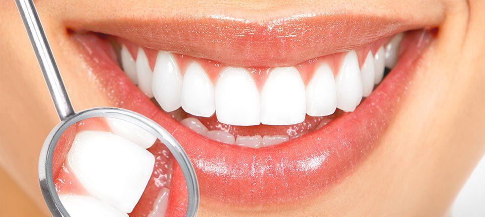 A dental mirror held against the mouth of a lady with dazzling white teeth and peach lipstick