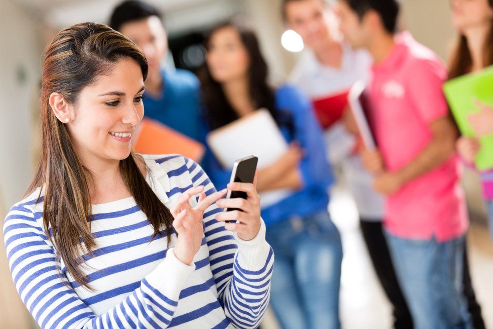 Una mujer usa un teléfono celular frente a un grupo de estudiantes.