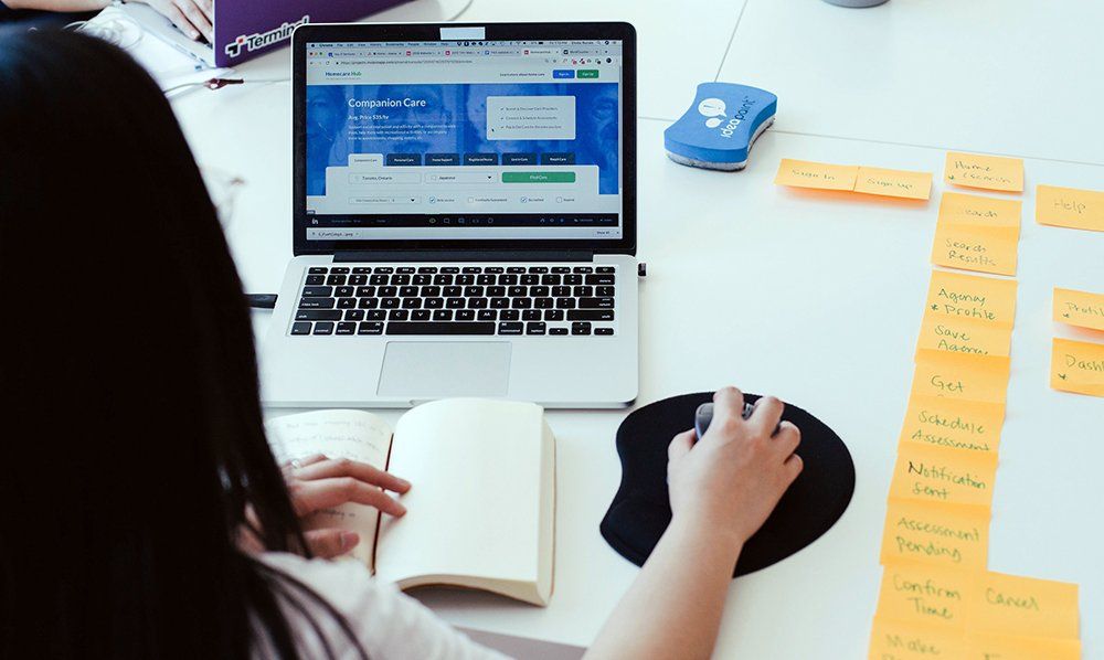Una mujer está sentada en una mesa usando una computadora portátil.