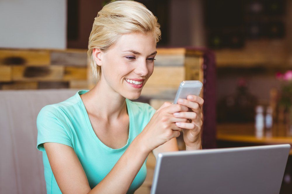Una mujer está sentada en una mesa usando una computadora portátil y un teléfono celular.