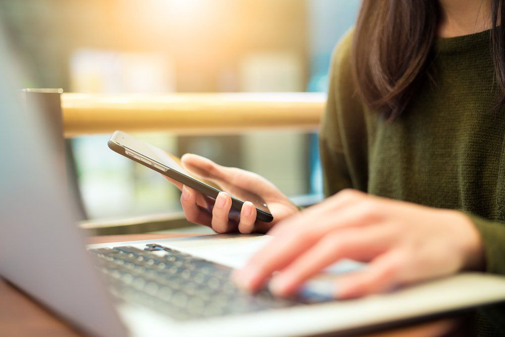 Una mujer está usando una computadora portátil y un teléfono celular.