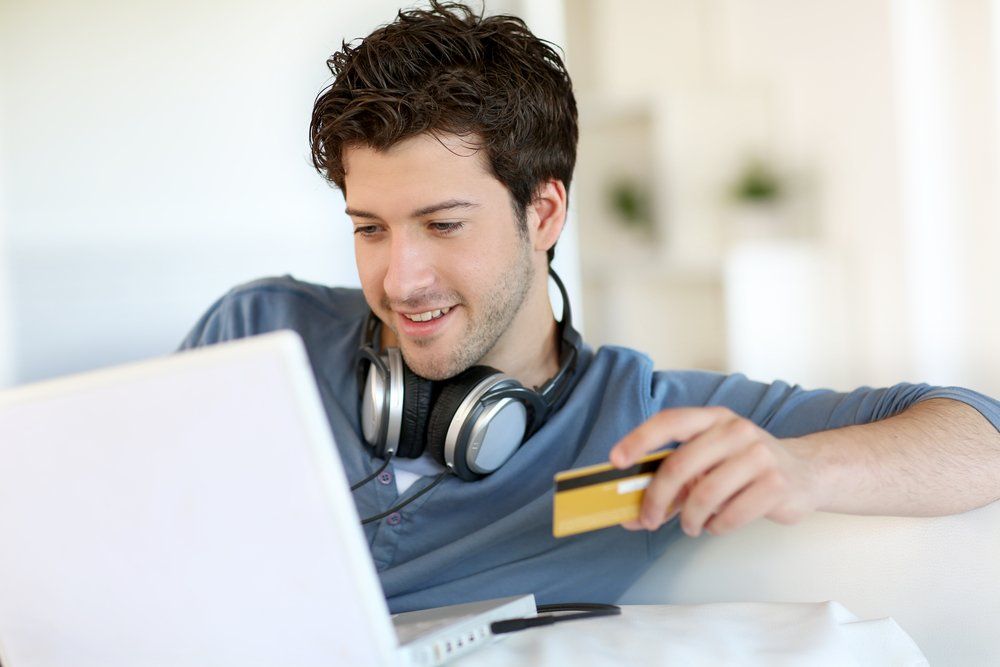 Un hombre que usa audífonos sostiene una tarjeta de crédito y usa una computadora portátil.