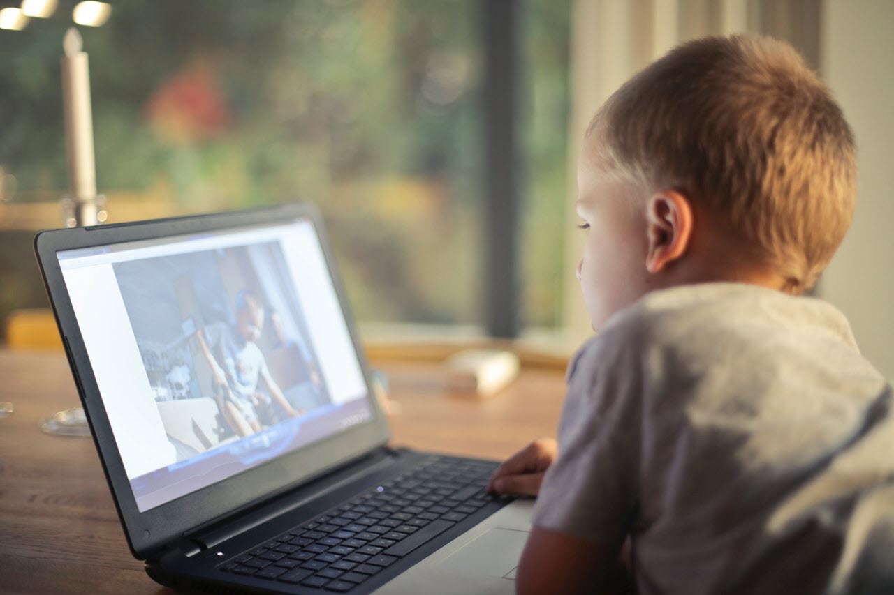 Un niño está sentado en una mesa usando una computadora portátil.