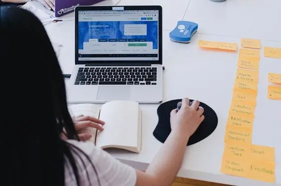 Una mujer está sentada en una mesa usando una computadora portátil.