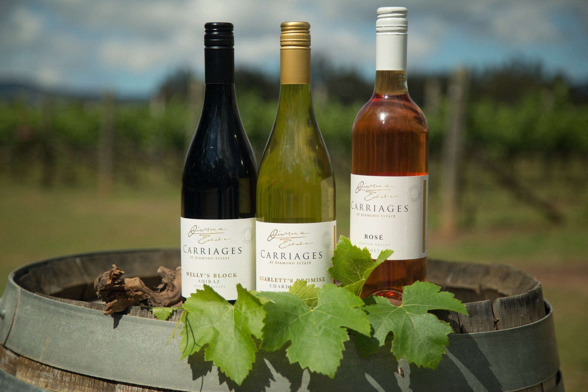 Three bottles of wine are sitting on top of a wooden barrel.