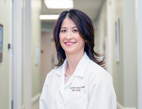 Woman in white lab coat smiles in a hospital hallway.