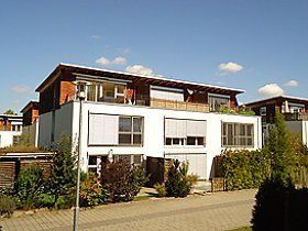 Ein großes weißes Haus mit vielen Fenstern ist von Bäumen und Büschen umgeben.