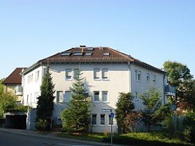 Ein großes weißes Gebäude mit einem braunen Dach und Bäumen davor.
