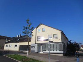 Ein großes weißes Haus mit einem Baum davor und einem blauen Himmel im Hintergrund.