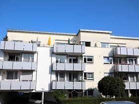 Ein weißes Mehrfamilienhaus mit Balkonen und einem davor geparkten Auto.