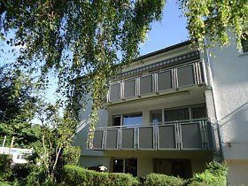 Ein weißes Haus mit Balkon und Bäumen davor.