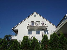 Ein großes weißes Haus mit einem Balkon und Bäumen davor.
