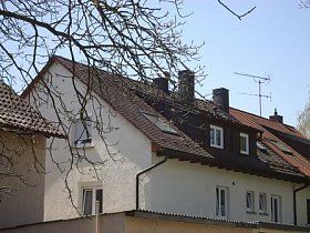 Ein weißes Haus mit einem braunen Dach und einer Satellitenschüssel auf dem Dach.