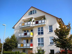 Ein weißes Wohnhaus mit Balkonen und einem blauen Himmel im Hintergrund.